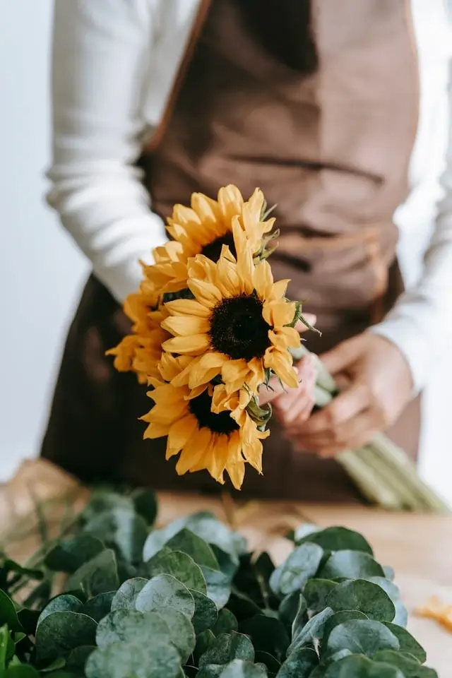 A florist making a bouquet with sunflowers and eucalyptus